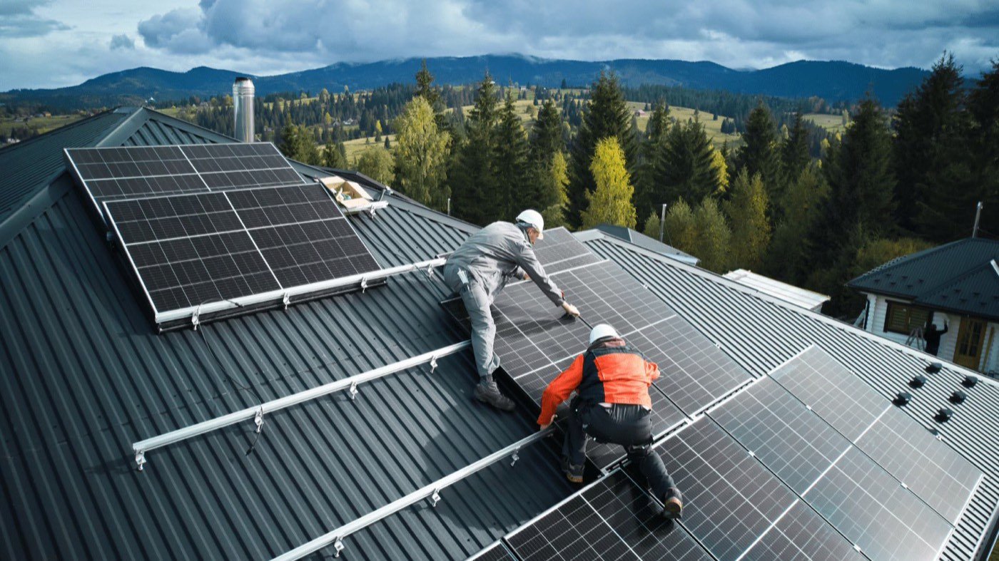 Deux installateurs fixant des panneaux photovoltaïques sur la toiture d’une maison, en région de montagne