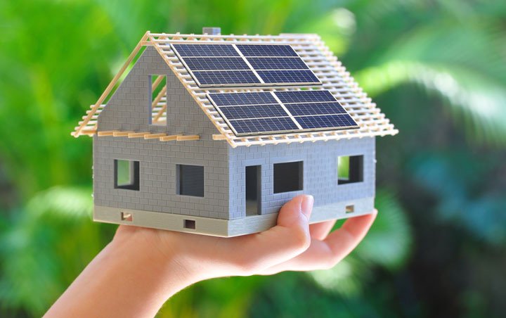 Maquette de maison dont la toiture est équipée de panneaux photovoltaïques, tenue dans une main