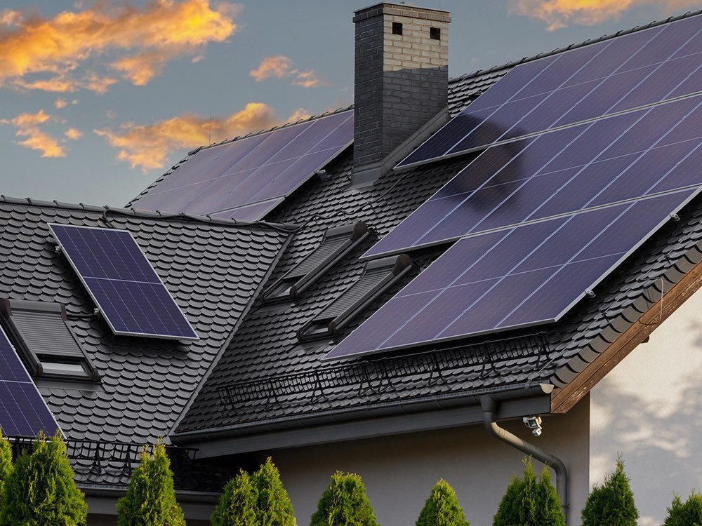 Toiture en tuiles noires équipée de panneaux photovoltaïques, au coucher du soleil