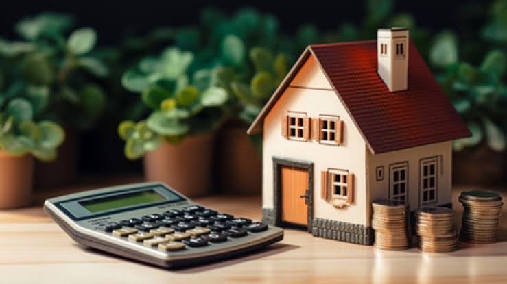 Maquette de maison individuelle posée à côté d’une calculatrice et de piles de pièces de monnaie